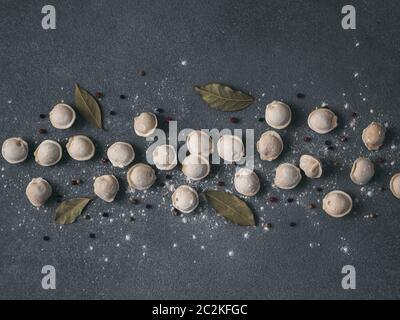 Schéma des pelmeni russes non cuits congelés avec des grains de poivre et les feuilles de laurier sur fond noir. Mise en page créative de boulettes. Belles matières épars Banque D'Images