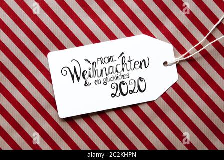 L'étiquette avec la calligraphie allemand Frohe Weihnachten und ein 2020 Glueckliches veut dire Joyeux Noël et une Bonne 2020. Papier d'emballage rouge en arrière-plan Banque D'Images