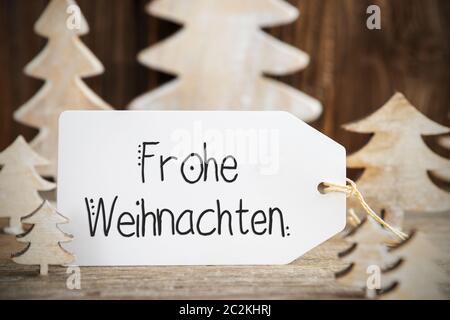 Une étiquette avec le texte allemand Frohe Weihnachten signifie joyeux Noël. Arbre de Noël en bois blanc comme décoration. Fond en bois brun Banque D'Images