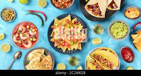 Un panorama de la cuisine mexicaine, de nombreux plats de la cuisine du Mexique, plat, top shot sur fond bleu. Nachos, tequila, guac Banque D'Images