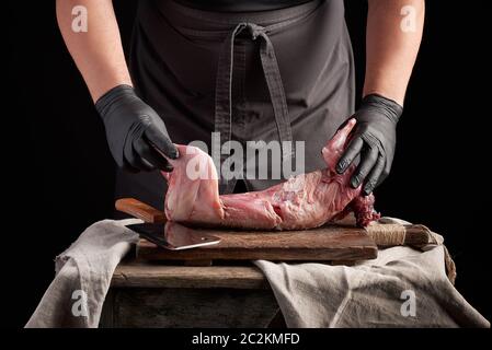Gants en latex noir en chef tient un lapin entier sur une carcasse brown à découper, processus de la cuisson des viandes Banque D'Images