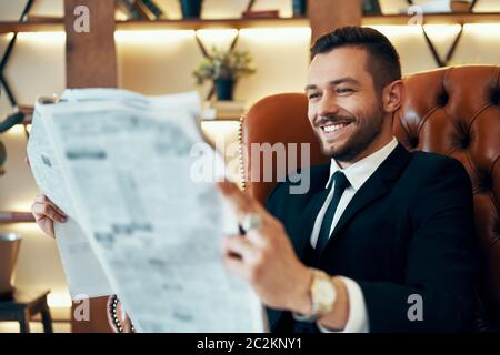 Un jeune homme d'affaires heureux lisant les journaux et les dernières nouvelles tout en étant assis dans un fauteuil Banque D'Images