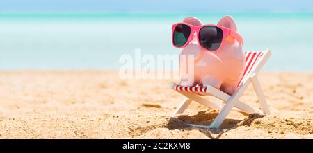 Pink Piggybank portant des lunettes sur une chaise longue sur la plage de sable Banque D'Images