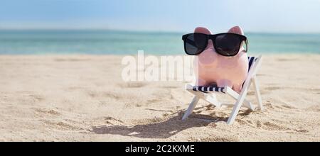 Pink Piggybank portant des lunettes sur une chaise longue sur la plage de sable Banque D'Images