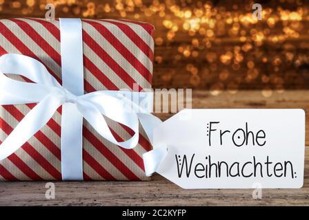 Un cadeau de Noël avec étiquette avec calligraphie allemand Frohe Weihnachten signifie joyeux Noël. Du papier d'emballage avec un arc et des lumières en arrière-plan Banque D'Images