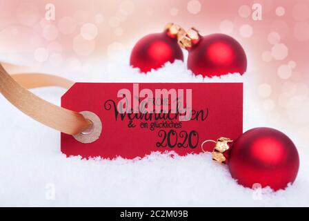 Label Rouge avec calligraphie allemand Frohe Weihnachten und ein Glueckliches 2020 dire Joyeux Noël et une Bonne 2020. Boule de noël ornement. Bokeh Ba Banque D'Images