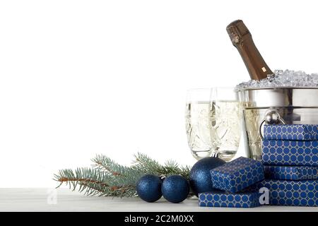 Encore vie avec bouteille de champagne debout dans un seau avec glace, flûtes à champagne, boîtes cadeaux, branche de sapin, décoration de Noël sur table en bois sur blanc Banque D'Images