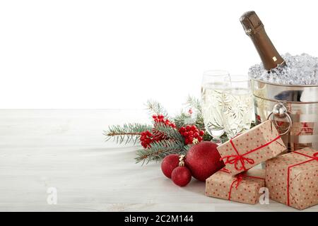 Encore vie avec bouteille de champagne debout dans un seau avec glace, flûtes à champagne, boîtes cadeaux, branche de sapin, décoration de Noël sur table en bois sur blanc Banque D'Images