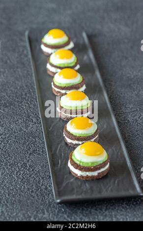 Canape avec fromage à la crème, guacamole et oeufs de caille frit sur la plaque Banque D'Images