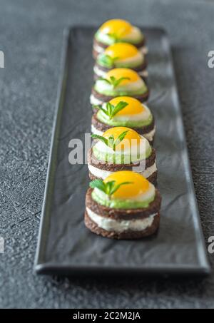 Canape avec fromage à la crème, guacamole et oeufs de caille frit sur la plaque Banque D'Images