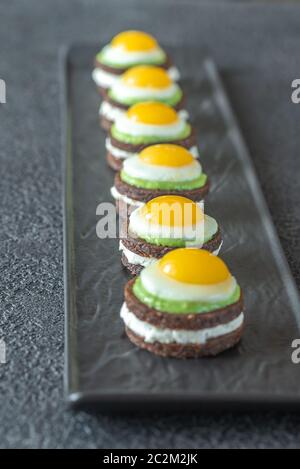 Canape avec fromage à la crème, guacamole et oeufs de caille frit sur la plaque Banque D'Images