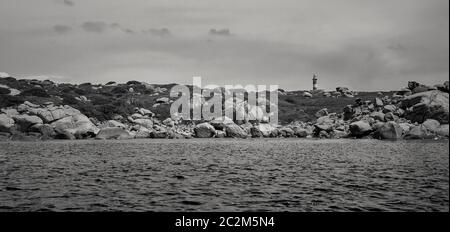 Leuchtturm niché dans un promontoire naturel mis au point à l'horizontale sous le liea et ciel nuageux pris dans au milieu de la mer. Image en blac Banque D'Images