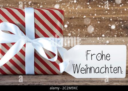 Un cadeau de Noël avec étiquette avec calligraphie allemand Frohe Weihnachten signifie joyeux Noël. Du papier d'emballage avec un arc et des flocons Banque D'Images