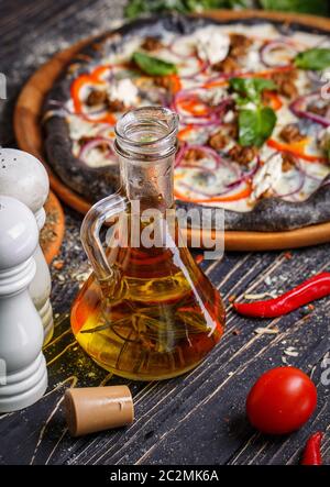 Pizza italienne avec pâte noire avec légumes en arrière-plan. L'huile d'olive, le sel, le poivre, les tomates et le poivre rouge à l'avant. Banque D'Images