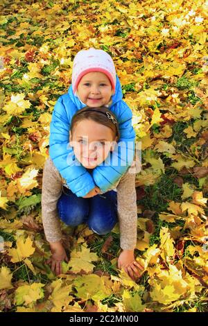 Les jeunes sœurs s'assoient et s'étreinte sur les feuilles jaunes dans le parc d'automne Banque D'Images