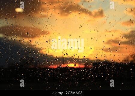 Pluie à l'extérieur de la fenêtre sur fond de coucher de soleil. La pluie tombe sur le verre pendant la pluie Banque D'Images