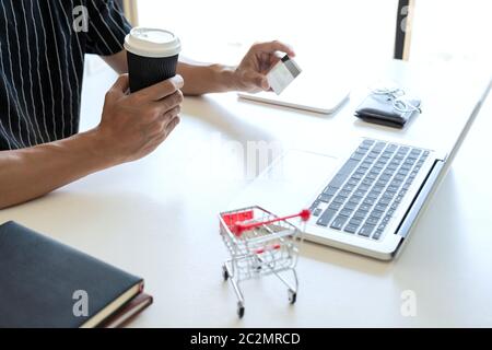 Homme tenant une carte de crédit en main et entrer le code de sécurité à l'aide de smart phone sur clavier d'ordinateur portable, le paiement en ligne shopping concept. Banque D'Images