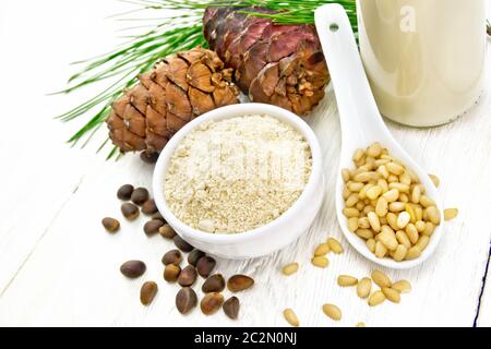 Farine de cèdre dans un bol, noix et cônes, une cuillère avec des noix épluchées, une branche de pin et du lait de cèdre dans une bouteille sur fond de planche en bois Banque D'Images