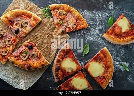 Tranches de pizza servies avec du fromage mozzarella, du jambon, des champignons et de la sauce tomate sur fond sombre Banque D'Images