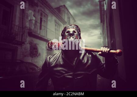 Homme psycho en colère dans un masque de hockey et un manteau en cuir noir avec une batte de baseball sanglante enveloppée d'une chaîne. Maniaque attendant sa victime la nuit ci Banque D'Images