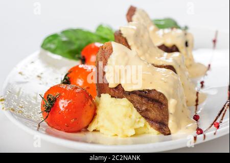 La viande de mouton au four avec sauce crémeuse, purée de pommes de terre et tomates cerises Banque D'Images