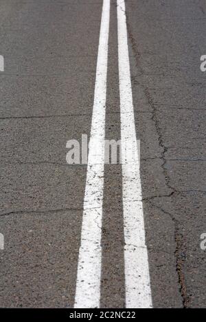 Texture d'une route asphaltée, avec une vue de dessus d'une double bande blanche Banque D'Images