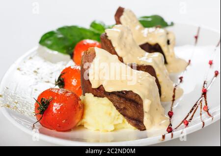 La viande de mouton au four avec sauce crémeuse, purée de pommes de terre et tomates cerises Banque D'Images