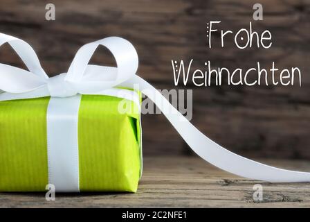 L'étiquette avec la calligraphie allemand Frohe Weihnachten signifie joyeux Noël. Un cadeau vert avec un arc. Fond en bois brun Banque D'Images
