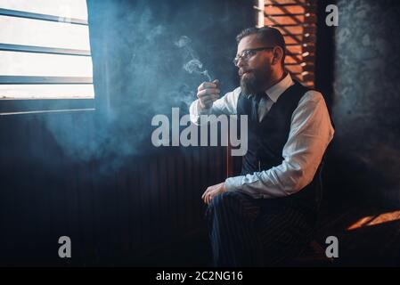 Portrait d'homme barbu à lunettes assis sur une chaise et le tabagisme. Écrivain, journaliste, auteur de la littérature, blogger ou poète concept Banque D'Images