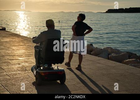 Couple senior marchant le long de la côte méditerranéenne - homme handicapé en fauteuil roulant Banque D'Images