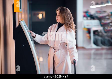 Jeune femme à l'aire de transfert en libre-service effectuant un auto-enregistrement ou achetant des billets d'avion dans le bâtiment moderne du terminal de l'aéroport Banque D'Images