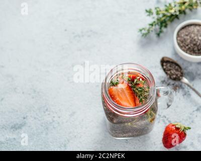 Vue depuis le dessus de l'eau de chia dans un pot de maçon avec fraise et thym sur fond de ciment gris. Eau de détox infusée de Chia avec baies. Copier l'espace pour tex Banque D'Images