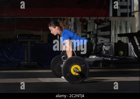 Jeune femme faisant soulevé de terre entraînement avec haltères lourds en salle de sport Banque D'Images