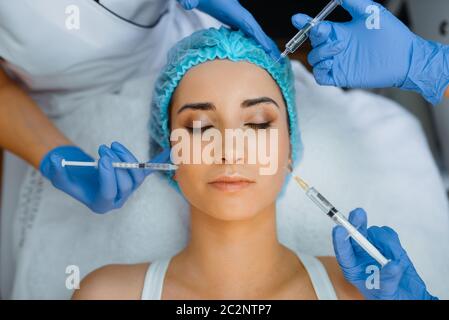 Les mains de la cosméticienne en gants maintiennent les seringues avec injection de botox sur le visage de la patiente. Procédure de rajeunissement dans le salon de beauté. Médecin et femme, Banque D'Images