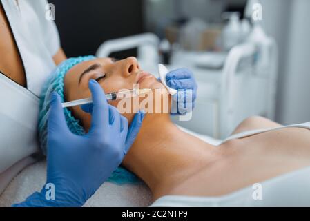 La cosméticienne en gants donne l'injection de botox de menton à la patiente sur la table de traitement. Procédure de rajeunissement dans le salon de beauté. Médecin avec seringue Banque D'Images