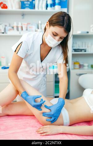 La cosméticienne en gants donne l'injection de botox dans la cuisse à la patiente sur la table de traitement. Procédure de rajeunissement dans le salon de beauté. Médecin et Banque D'Images