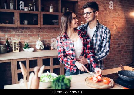 Mari hugs femme pendant qu'elle la cuisson dans un bol à salade de légumes frais sur la cuisine. Le régime alimentaire la préparation des aliments. Couple prépare un dîner romantique, vie saine Banque D'Images