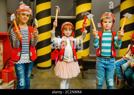 Enfants en casques et uniforme avec des outils dans les mains jouant pompier, salle de jeux à l'intérieur. Enfants lerning profession. Garçons et filles joue sauveteurs, littl Banque D'Images