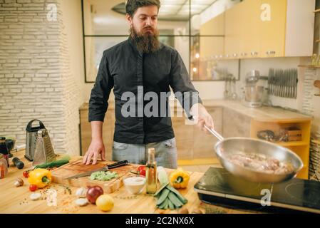 Male chef cooking meat avec vetables dans la poêle sur la cuisine. L'homme préparer la viande bovine Banque D'Images