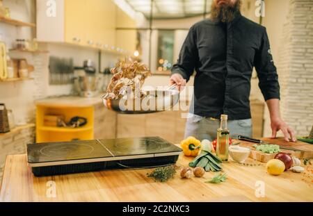 Un chef cuisinier cuisant de la viande avec des produits en vetables dans la poêle de la cuisine. Homme préparant du boeuf sur table cuisinière électrique Banque D'Images