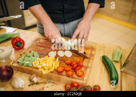 Chef de la main d'entaille les champignons sur planche en bois libre. Homme couper des légumes sur le comptoir de cuisine, une salade fraîche, cuisine intérieur sur arrière-plan. Banque D'Images