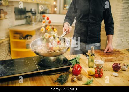 Un chef cuisinier cuisant de la viande avec des produits en vetables dans la poêle de la cuisine. Homme préparant du boeuf sur table cuisinière électrique Banque D'Images