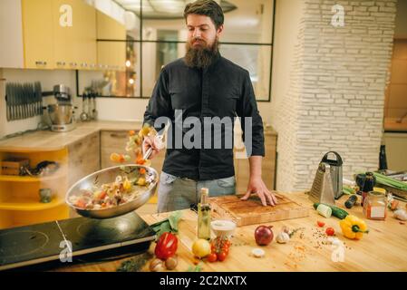 Male chef cooking meat avec vetables dans la poêle sur la cuisine. L'homme préparer la viande bovine Banque D'Images