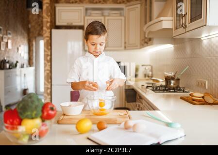 Le petit garçon agite les œufs crus dans un bol, préparation de pâtisserie. Cuisine pour enfants. Un enfant heureux prépare un dessert sucré Banque D'Images