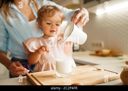 La jeune mère et l'enfant verse du lait dans un verre, ingrédients pour la pâtisserie. Femme et petite fille cuisant sur la cuisine, préparation de gâteau. Bonne famille mak Banque D'Images