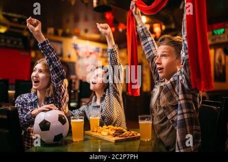 Fans de football avec écharpe regarder match et lever la main jusqu'au bar des sports. La diffusion Tv, jeunes amis loisirs en pub, équipe favorite gagne Banque D'Images