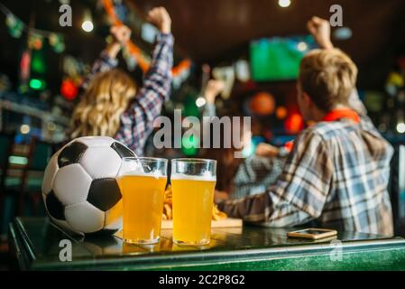 Ball et de la bière sur la table dans un bar sportif, les fans de football sur l'arrière-plan. La diffusion TV, regarder le jeu concept Banque D'Images