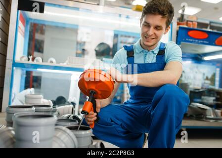 Technicien sanitaire en uniforme dans la vitrine du magasin de plombage. Plombier achetant plombier dans l'atelier, tuyaux d'égout et d'adaptateurs choix Banque D'Images