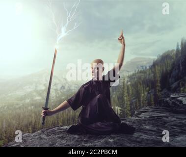 Maître de Wushu avec blade, le contrôle de la foudre sur le sommet de la montagne, les arts martiaux en homme tissu noir pose avec épée Banque D'Images