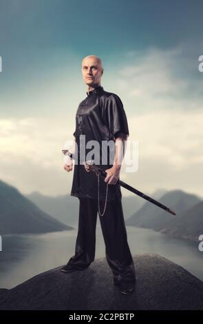 Maître de Wushu avec épée pose sur le sommet de la montagne, les arts martiaux en homme tissu noir pose avec lame Banque D'Images